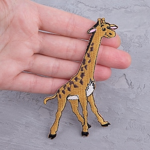 May include: Embroidered giraffe patch. The giraffe has a tan body, brown spots, and black accents. It features a long neck and legs, with a white patch on its side. Suitable for clothing or accessories.
