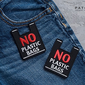 May include: Two black and white embroidered patches with the text "NO PLASTIC BAGS" in red and white lettering. The patches are sewn onto a pair of blue denim jeans.