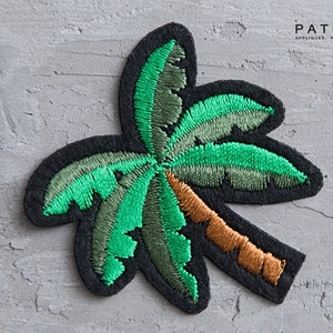 May include: Green embroidered palm tree patch with a brown trunk. The patch is on a gray textured background.