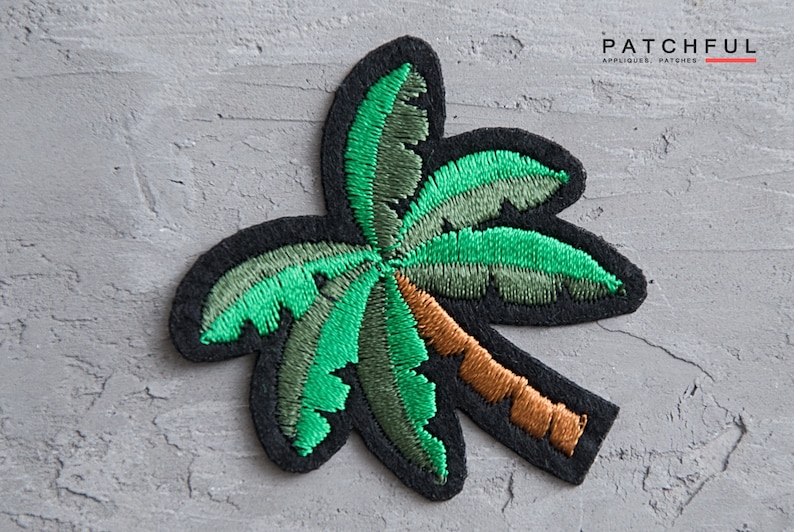 May include: Green embroidered palm tree patch with a brown trunk. The patch is on a gray textured background.