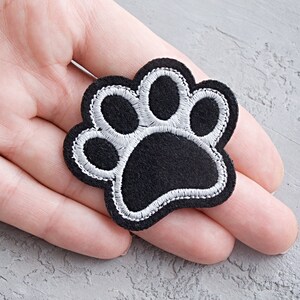 May include: A black felt paw print with white stitching. The paw print is about 2 inches wide.