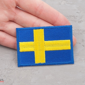 Puede incluir: Un parche bordado con la bandera de Suecia, con fondo azul y una cruz amarilla.