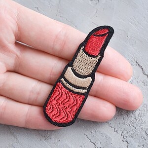 May include: Red and beige embroidered iron-on patch of a lipstick tube.