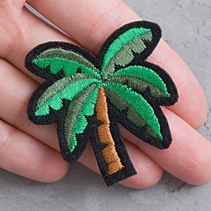 May include: Green and brown embroidered palm tree patch. The patch is on a grey background.