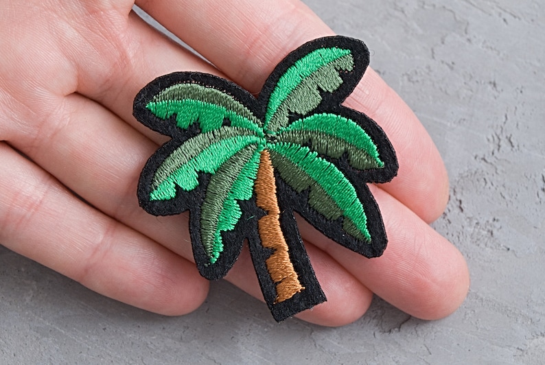 May include: Green and brown embroidered palm tree patch. The patch is on a gray background.