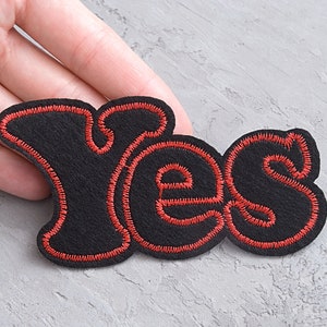Op de afbeelding: Zwarte viltpatch met rode stiksels in de vorm van het woord "Ja".
