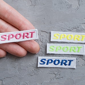 May include: Four white rectangular patches with the word "SPORT" embroidered in different colours: pink, yellow, light green, and blue.