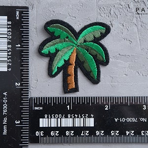 May include: A green and brown embroidered palm tree patch, measuring approximately 1 inch in width and 1.5 inches in height. The patch is on a gray textured surface with a ruler for scale.