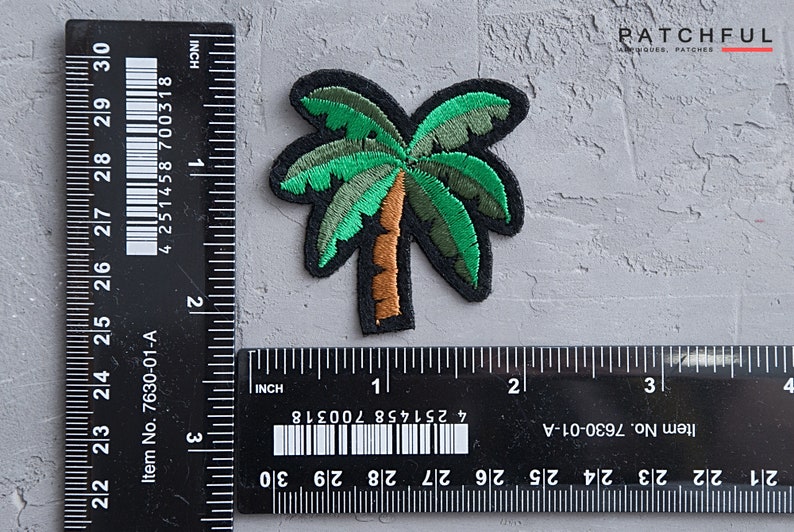 May include: A green and brown embroidered palm tree patch, measuring approximately 1 inch in width and 1.5 inches in height. The patch is on a gray textured surface with a ruler for scale.