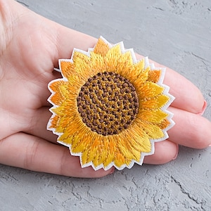 Könnte beinhalten: Ein gelber gestickter Sonnenblumen-Patch mit brauner Mitte. Der Patch ist auf weißem Hintergrund.
