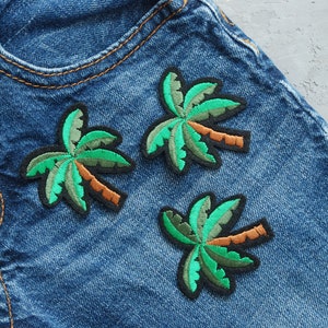 May include: Three green palm tree embroidered patches on a blue denim background.