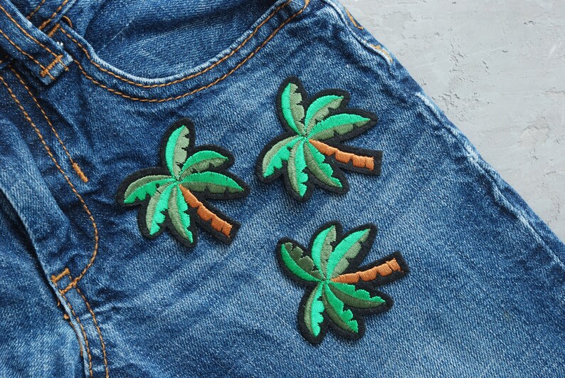May include: Three green palm tree embroidered patches on a blue denim background.