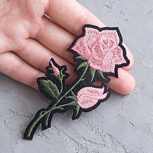 Könnte beinhalten: Rosa gestickter Rosenblumen-Patch mit grünen Blättern und schwarzem Stiel.