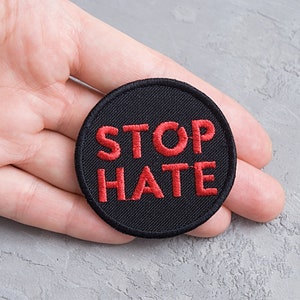 Op de afbeelding: Een ronde zwarte patch met rode geborduurde tekst die "STOP HATE" zegt.