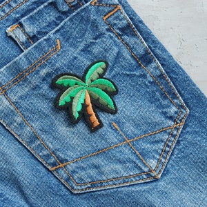 May include: A blue denim jean pocket with a green and brown palm tree patch sewn on it.