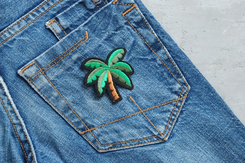 May include: A blue denim jean pocket with a green and brown palm tree patch sewn on it.