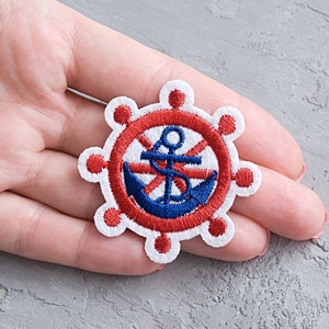 Peut inclure: Un patch en feutre blanc avec une ancre et un volant brodés en rouge et bleu.