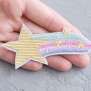 Könnte beinhalten: Ein gelber Stern mit einem Regenbogen-Schwanz und kleinen weißen Sternen. Der Patch ist gestickt und hat einen weißen Umriss.