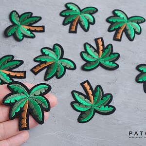May include: Nine green embroidered palm tree iron-on patches. The patches are on a gray textured surface. The patches are approximately 2 inches in size.