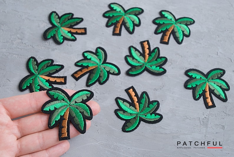 May include: Nine green embroidered palm tree iron-on patches. The patches are on a gray textured surface. The patches are approximately 2 inches in size.