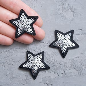 Puede incluir: Tres parches en forma de estrella con lentejuelas plateadas y bordes de tela negra.