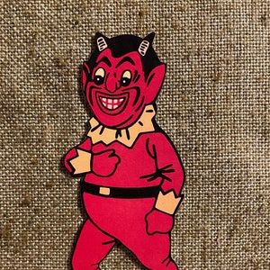 May include: A red cartoon devil with horns, a wide grin, and a black and white face. The devil is wearing a red suit with a white collar and black shoes.