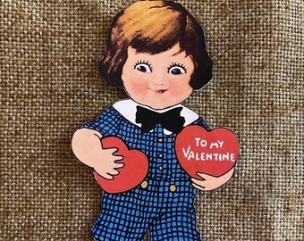 May include: A vintage Valentine's Day card featuring a cartoon boy wearing a blue and white checkered shirt and holding two red hearts. One heart says "To My Valentine".