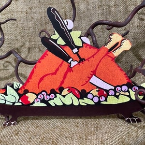 Puede incluir: Un recorte de papel de un pavo de Acción de Gracias con una salsera marrón y una guarnición verde y roja. El pavo es naranja y rojo con un cuchillo y un tenedor blancos.