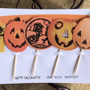 May include: A set of six Halloween-themed cupcake toppers featuring orange and black jack-o'-lantern faces, a witch flying on a broomstick, a haunted house, and the word "Treat". The toppers are on wooden skewers and are labeled "No. 3".