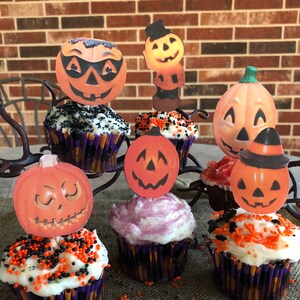 May include: A collection of Halloween cupcakes decorated with orange and black sprinkles. The cupcakes are topped with various Halloween-themed cutouts, including pumpkins, ghosts, and bats.