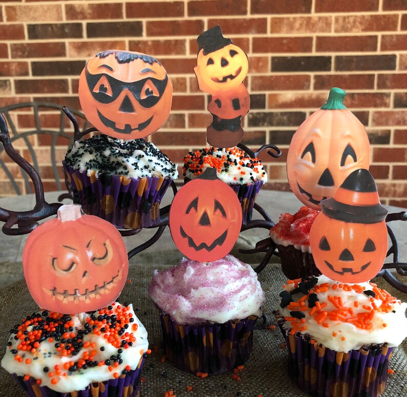 May include: A collection of Halloween cupcakes decorated with orange and black sprinkles. The cupcakes are topped with various Halloween-themed cutouts, including pumpkins, ghosts, and bats.