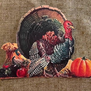 Puede incluir: Un recorte de pavo de Acción de Gracias de papel vintage con un diseño colorido. El pavo está de pie junto a una calabaza y otros artículos de la cosecha de otoño.