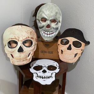 May include: Four Halloween skull masks, two are white with black eyes and a black mouth, one is beige with black eyes and a black mouth, and one is beige with black eyes and a black mouth and a black hat.