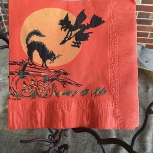 May include: Orange paper napkin with a black cat, a witch flying on a broomstick, and two jack-o'-lanterns. The background is a large orange circle with a yellow center. The text "Van Ness" is printed in the bottom left corner.