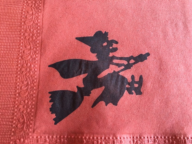 May include: A black silhouette of a witch flying on a broomstick against a red background. The witch is wearing a pointed hat and has a long flowing cape.