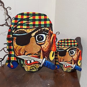 Op de afbeelding: Twee kartonnen piratenmaskers met een geruit patroon, een grote en een kleine. Beide maskers hebben een ooglap, een mes en een gouden oorring.