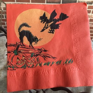 May include: Orange Halloween paper napkin with a black cat, a witch flying on a broomstick, and pumpkins. The napkin has a decorative border and the text "Van Ness" in the bottom left corner.