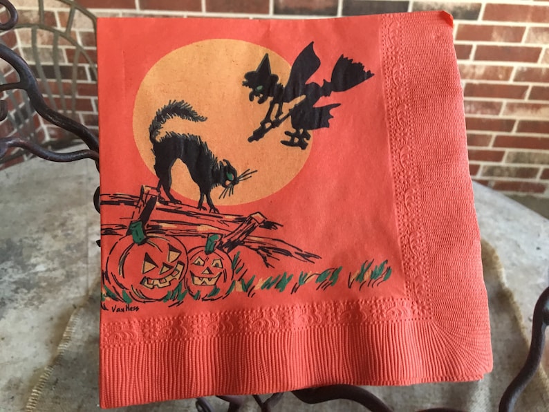 May include: Orange Halloween paper napkin with a black cat, a witch flying on a broomstick, and pumpkins. The napkin has a decorative border and the text "Van Ness" in the bottom left corner.