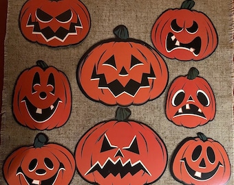 May include: Eight orange paper jack-o'-lantern cutouts with different facial expressions. The jack-o'-lanterns are all the same size and shape, and they are arranged in a circle.