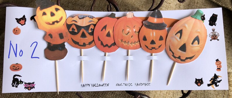 May include: Set of six Halloween cupcake toppers featuring various pumpkin faces with different expressions. The toppers are made of paper and have wooden sticks attached to the back. The card reads "Happy Halloween" and "Non-toxic Handmade".