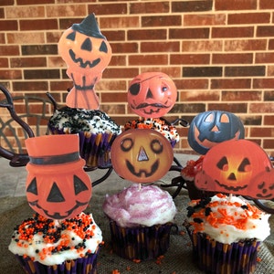 May include: Six Halloween cupcakes decorated with orange and black sprinkles. Each cupcake has a different vintage-style pumpkin face topper.