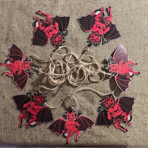 May include: A string of seven red devil Halloween decorations with black wings and a black and white string.