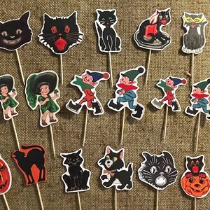 以下が含まれることがあります： 黒猫、魔女、ゴブリンをモチーフにしたハロウィンカップケーキのデコレーション16個セット。デコレーションは厚紙に印刷され、木製串に付けられています。