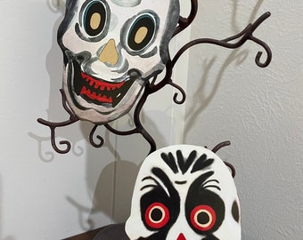 Könnte beinhalten: Zwei Halloween-Masken, eine weiße mit einem schwarzen Totenkopf-Design und roten Augen und die andere schwarze mit einem weißen Totenkopf-Design und roten Augen.