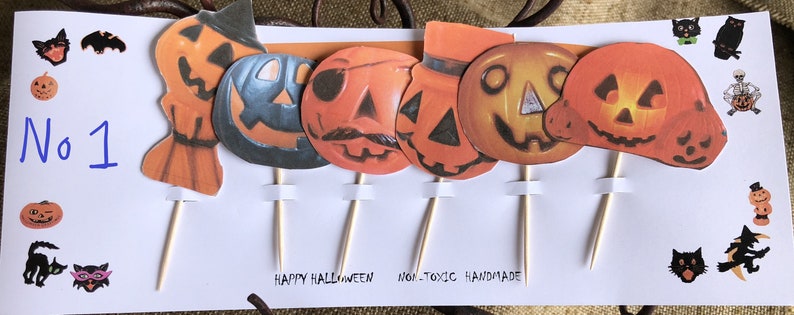 May include: Set of six Halloween cupcake toppers featuring various pumpkin designs with different facial expressions. The toppers are made of paper and have wooden sticks. The text "Happy Halloween - Non-Toxic Handmade" is written on the white background.
