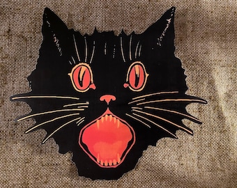 May include: A black cat with orange eyes and a wide open mouth, showing sharp teeth. The cat's fur is black and the background is a brown hessian texture.