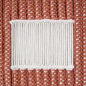 Puede incluir: Primer plano de un tapiz de macram&eacute; de pared con una secci&oacute;n rectangular blanca en el centro. El tapiz de pared est&aacute; hecho con cord&oacute;n marr&oacute;n y blanco.