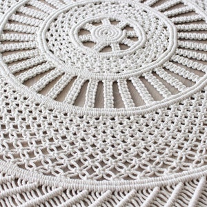 Peut inclure: Une suspension murale en macram&eacute; blanche avec un motif circulaire et des franges. Le macram&eacute; est r&eacute;alis&eacute; avec un cordon de coton naturel et pr&eacute;sente un motif d&eacute;licat et complexe.