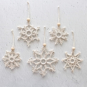 May include: Six white macrame snowflake ornaments with wooden beads hanging from white string.