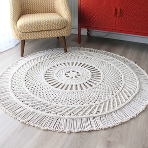 Peut inclure: Un tapis rond en macram&eacute; blanc avec une bordure en franges. Le tapis a un motif circulaire au centre et un design g&eacute;om&eacute;trique rayonnant vers l'ext&eacute;rieur.